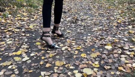 A girl in high-heeled shoes walks through the forest where there is a lot of dirt, she gets her heels dirty and enjoys it